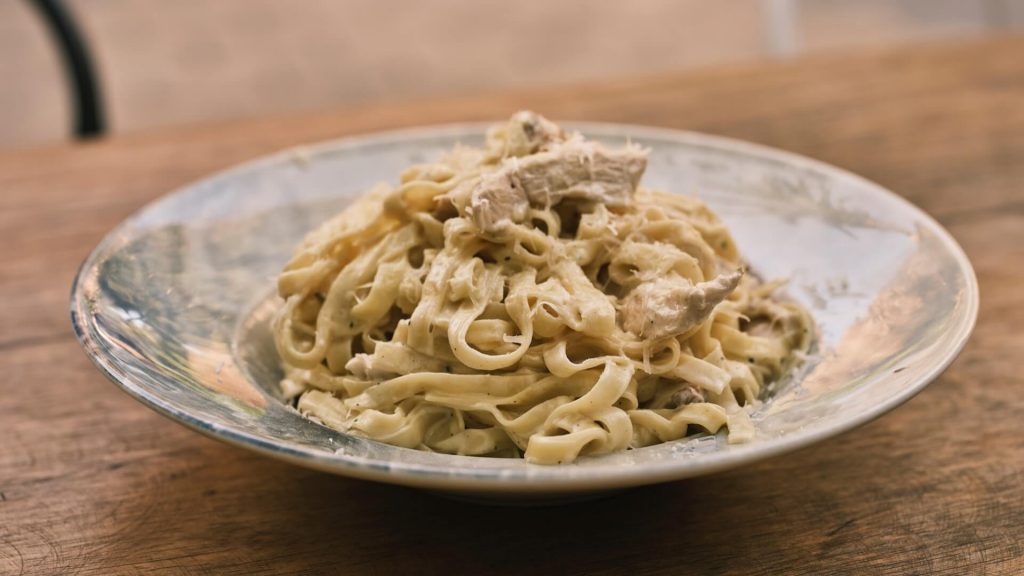A plate of pasta generously coated in creamy alfredo sauce, often garnished with parmesan cheese and parsley.