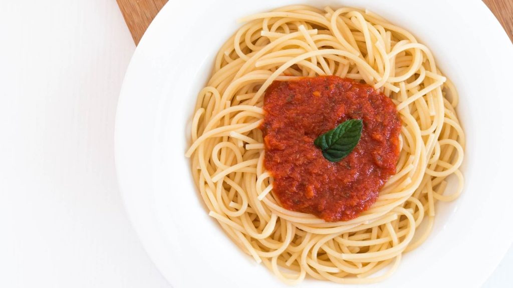 A plate of cooked pasta covered in savory marinara sauce, garnished with fresh basil leaves.