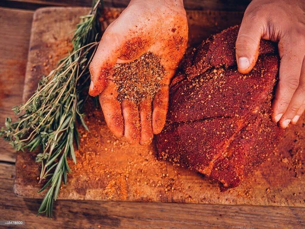 A person applying a coffee-infused meat rub to a piece of meat, enhancing its flavor and creating a savory delight.