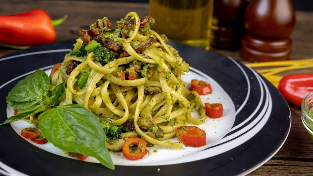 Pasta adorned with vibrant green pesto sauce, typically garnished with pine nuts and grated parmesan cheese.